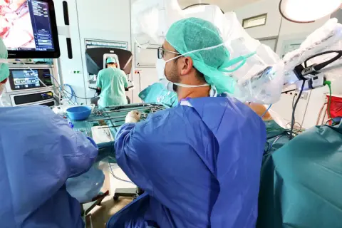 Chirurgen im OP-Saal bereiten sich auf eine onkologische Chirurgie vor, mit Fokus auf einem Monitor, der das Operationsfeld zeigt.