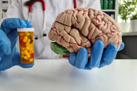 Lekarz w niebieskich rękawiczkach trzyma model mózgu i buteleczkę z lekami, sugerując jak odbudować mózg po depresji.
