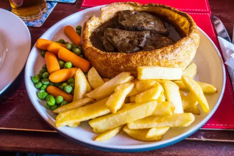 Pyszne danie kuchni brytyjskiej: pieczeń wołowa w Yorkshire puddingu, podana z frytkami, groszkiem i marchewką.