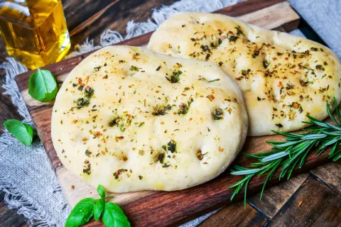 Zwei knusprige pizzabrote mit knoblauch und Kräutern, garniert mit frischem Rosmarin und Basilikum.