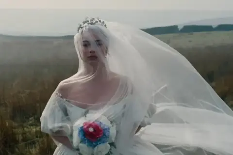 Panna młoda w welonie i koronie na tle wietrznego krajobrazu. Jak w Wichrowych Wzgórzach, jej los splata się z dziką naturą.