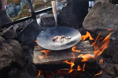 Kolbulle smet fräser i stekpannan över öppen eld. En klassisk fjällmåltid tar form.