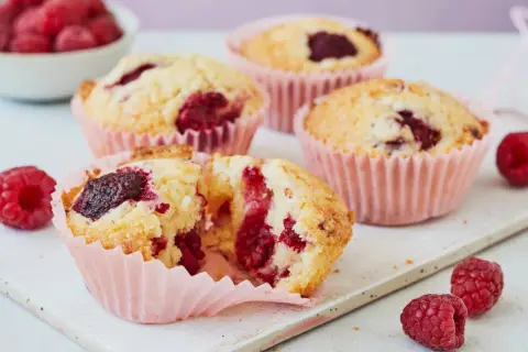 Saftige Himbeer Muffins in rosa Förmchen, mit frischen Himbeeren garniert. Ein Genuss!