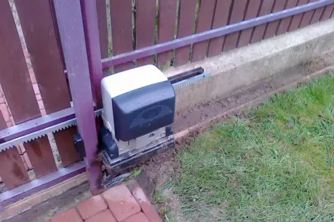 Silnik bramy przesuwnej, która po zamknięciu sama się otwiera, z widocznym zębatką i mechanizmem.