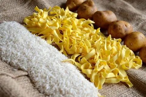 Reis, Nudeln und Kartoffeln liegen auf Jute. Was hat mehr Kalorien, Reis oder Kartoffeln? Die Antwort ist nicht so einfach.