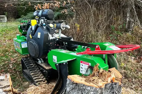 Grön stubbfräs med larvfötter redo att ta bort en stubbe i skogen.