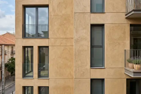 Fachada moderna con textura de arena, ventanas oscuras y balcones. El mejor mortero para fachadas exteriores protege esta construcción.