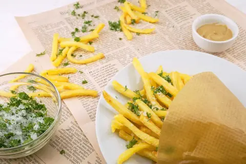 Des frites dorées, saupoudrées de persil et de sel, servies dans un cornet en papier. À côté, un bol de sel et de persil, et une petite coupelle de moutarde. Un délice qui rappelle les sardines frites.