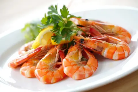 Deliciosas gambas al ajillo servidas en un plato blanco, adornadas con perejil fresco y rodajas de limón.