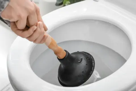 Main d'une personne utilisant une ventouse pour déboucher un WC.