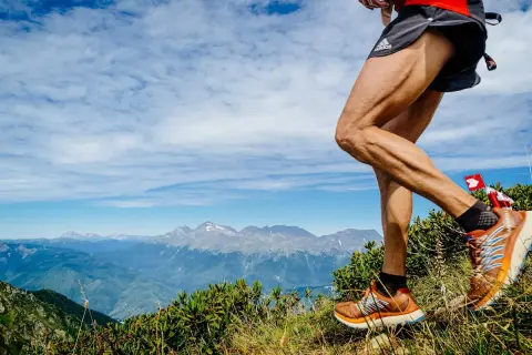 Un coureur en pleine descente trail sur un sentier de montagne, avec des sommets enneigés en arrière-plan.