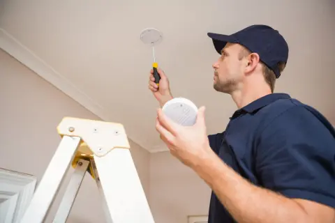 Un technicien installe des alarmes incendie au plafond, assurant la sécurité de votre domicile.