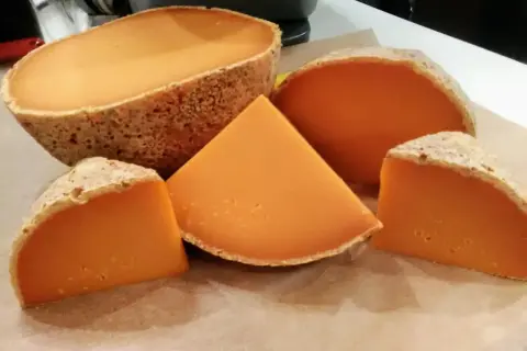 Un queso mimolette peligroso, con su corteza rústica y su vibrante interior anaranjado, se presenta en cuñas y una pieza entera, invitando a una degustación audaz.