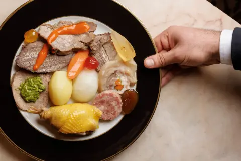 Un piatto ricco di bollito di carne, con verdure, salumi e un pollo arrosto, pronto per essere gustato.