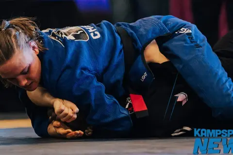 Två kvinnor i blå och svarta gi tävlar i bjj sm. En kämpar sig framåt, fokuserad på att vinna.