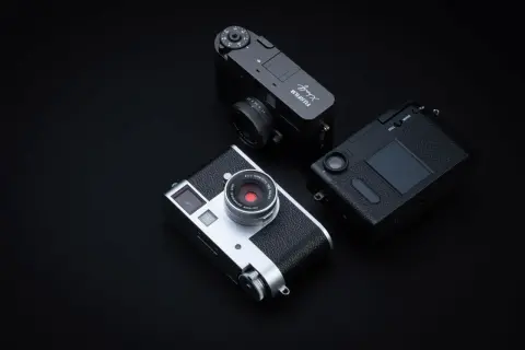 Tre fotocamere Fujifilm X-Half, una argento e due nere, disposte su sfondo scuro.