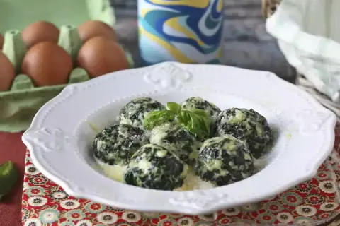 Spenat recept: Krämiga spenatbollar med basilika och parmesan på en vit tallrik. Ägg i bakgrunden.