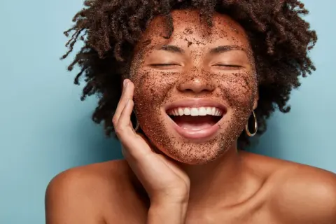 Mujer sonríe con la cara cubierta de un exfoliante, mostrando lo que es exfoliar la piel para una tez radiante.