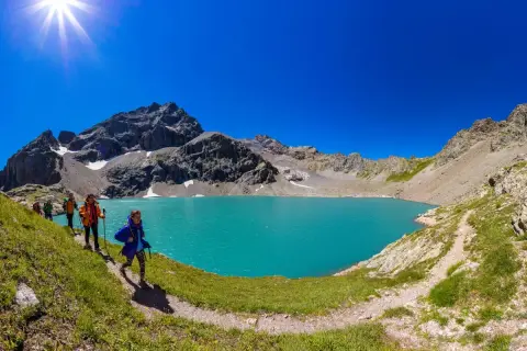 Randonneurs découvrant le magnifique lac de l'Eychauda, aux eaux turquoise vives, sous un ciel d'azur éclatant.