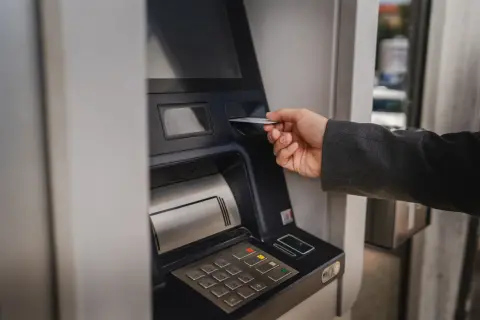 Dłoń wsuwa kartę do bankomatu, by sprawdzić, ile można wypłacić.