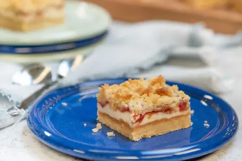 En bit rabarber cheesecake med smuldeg på en blå tallrik.