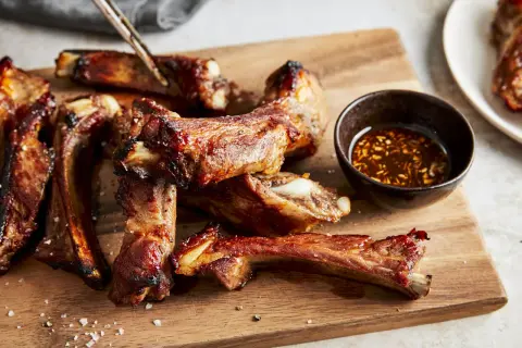 Saftige schweinerippchen braten, glasiert und mit Dip auf Holzbrett. Perfekt zum Genießen!