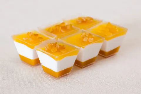 Sechs kleine Dessertgläser mit weißer Creme und Mango-Topping, garniert mit kleinen Fruchtstückchen.