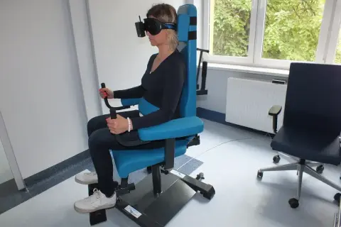Kobieta w goglach VR na specjalnym fotelu wykonuje badanie vng. Gdzie zrobić takie badanie?