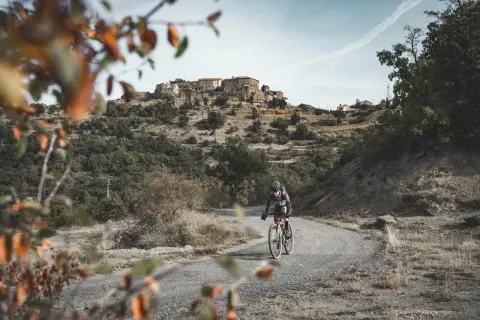 Ciclista en ruta de gravel, disfrutando del paisaje montañoso y el pueblo al fondo. Una aventura de montsec bikepacking loop.