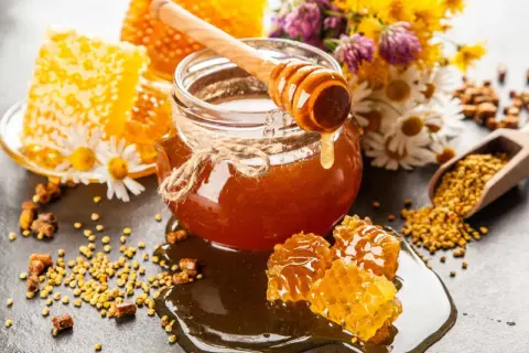 En burk gyllene honung, honungskaka och bipollen. Honung nyttigt för hälsan, omgiven av blommor.