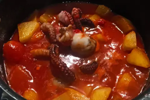 Un saporito stufato di polpo e patate in un sugo rosso brillante. I tentacoli del polpo sono ben visibili, immersi tra i pezzi dorati di patate.