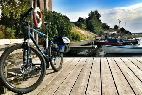 Rower z sakwami czeka na przygodę w Karlskronie. Drewniany pomost, łodzie i błękitne niebo zapraszają do odkrywania uroków wybrzeża.