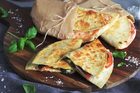 Läckra piadina recept på en träskärbräda, inslagna i papper med snöre. Basilika och flingsalt dekorerar.