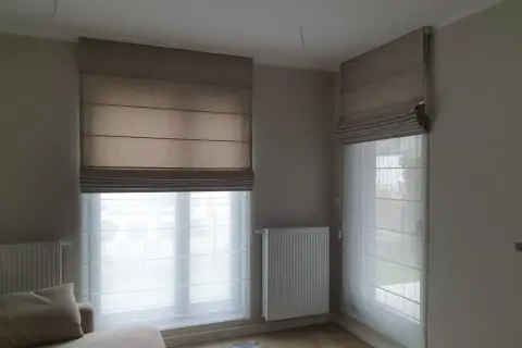 Eleganckie rolety rzymskie i zasłony tworzą przytulną atmosferę w pokoju.