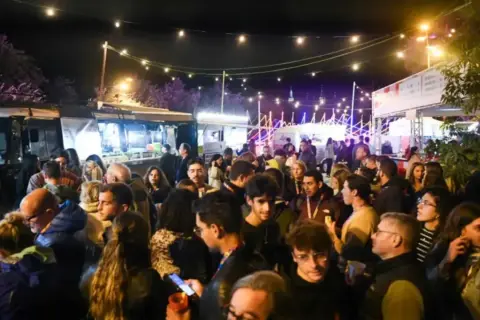Multitud disfrutando de food trucks Zaragoza Pilares bajo luces festivas.