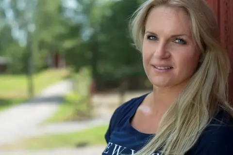 Frida, en stark frida boxare, ler mot kameran. Bakom henne syns en grönskande sommaridyll.