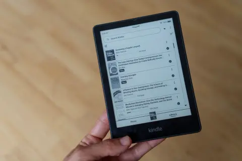 Main d'une personne tenant un livre format Kindle affichant une liste de titres, dont "Becoming a Supple Leopard" et "The Lean Startup".