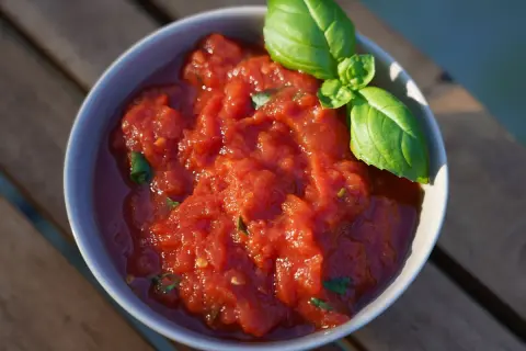Schüssel mit frischer, stückiger Tomatensoße, wie in der Pizzeria, garniert mit Basilikum. Perfekt für hausgemachte Pizza.