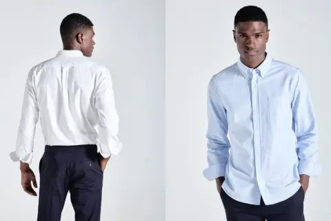 Ein Mann präsentiert ein weißes und ein hellblaues Button-Down-Hemd. Dieses Hemd mit Knopfleiste ist ein Klassiker.
