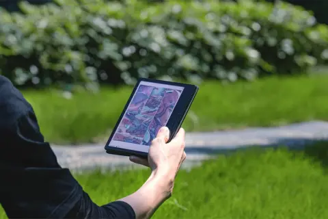 Une personne lit une bande dessinée de science-fiction sur une liseuse Boox dans un parc verdoyant.