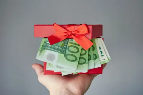 Czerwone pudełko z prezentem i banknotami euro na dłoni.