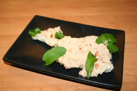 Zarter Fisch mit cremiger Joghurtsoße, garniert mit frischen Kräutern auf schwarzer Platte.