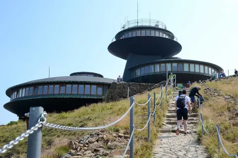 Wanderer steigen die Steintreppe zur Schneekoppe Seilbahn hinauf. Die futuristischen Gebäude auf dem Gipfel sind schon zu sehen.