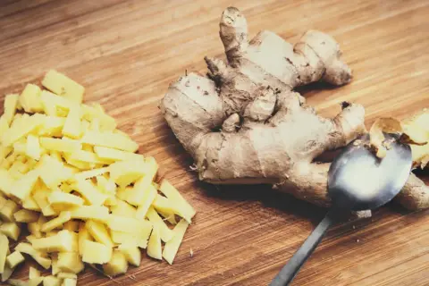 Pokrojony imbir i całe korzenie na desce. Łyżka obok, gotowe do jedzenia imbiru.