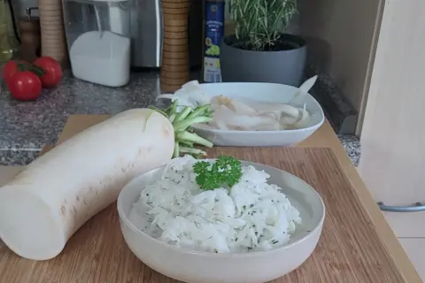 Ein frischer Rettich liegt neben einer Schüssel mit cremigem Rettichsalat, garniert mit Petersilie. Perfekt für ein leichtes Rettichsalat Rezept.