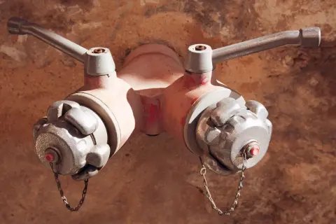 Czerwony hydrant podziemny z dwoma metalowymi zaworami i łańcuszkami, gotowy do akcji.