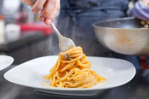 Eine Gabel hebt dampfende Spaghetti, ein Klassiker der Pasta italiana, auf einen weißen Teller.
