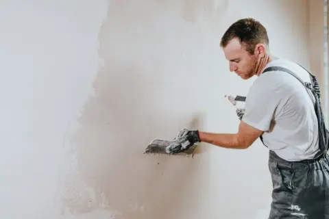 Operaio con spatola applica intonaco su muro. La rasatura è un passaggio cruciale per una finitura perfetta.
