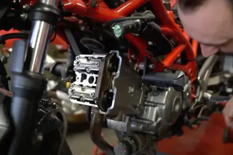 Mechanik pracuje nad silnikiem motocykla, pokazując, jak ustawić zawory.