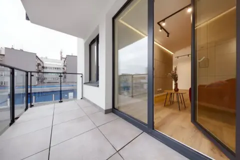 Nowoczesny balkon z płytkami, szklaną balustradą i widokiem na budynki.